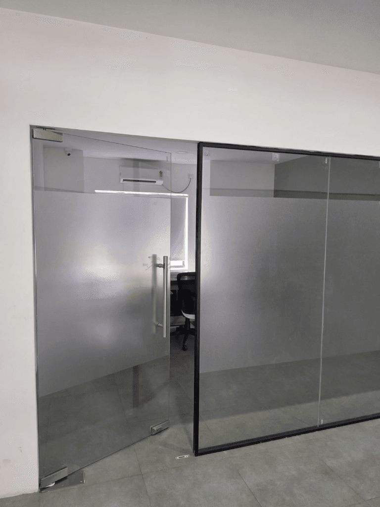 Glass door with a steel handle opening into a cabin with a desk and chair